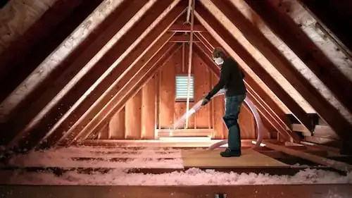 A worker blowing pink insulation across an attic floor