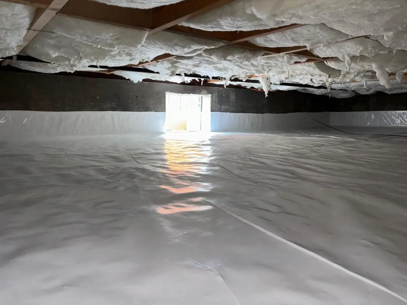 A finished crawlspace with white insulation batts overhead and a sealed vapor barrier floor